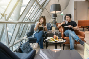 ALT="Asian woman and Asian man eating food in airport lounge showing how airlines engaging in customer loyalty"